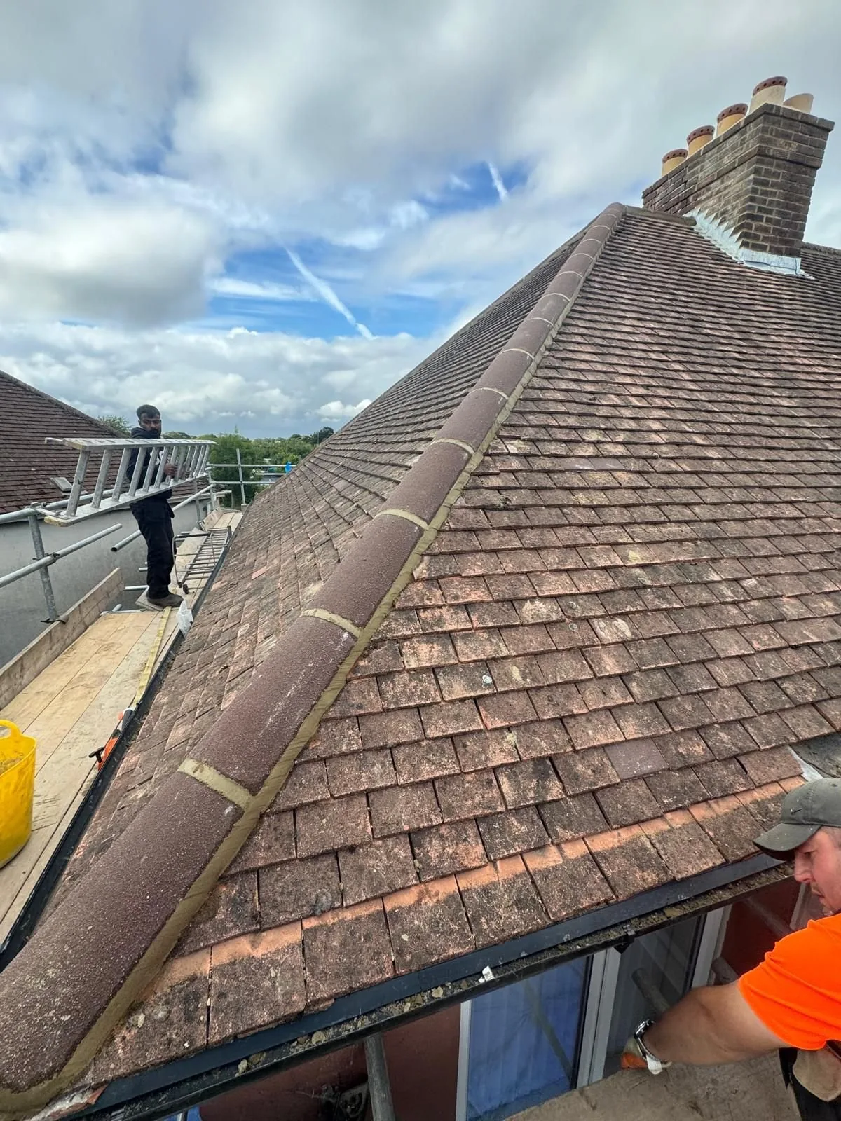 Rayner’s Roofing team repairing hip tiles on a clay plain-tile roof from scaffold