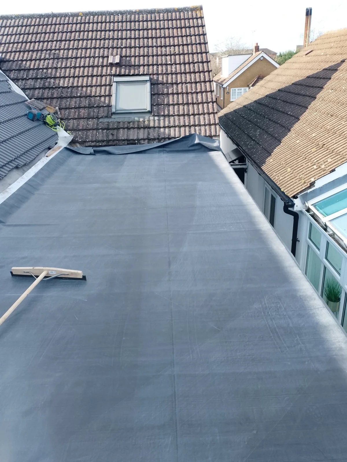 Completed EPDM rubber flat roof on a home extension with tiled roofs behind
