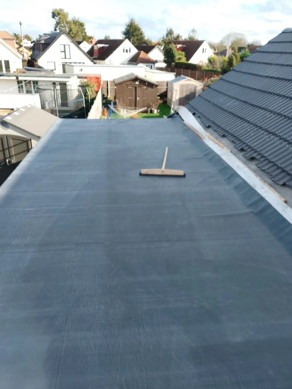 Newly installed EPDM rubber flat roof beside a pitched tiled roof